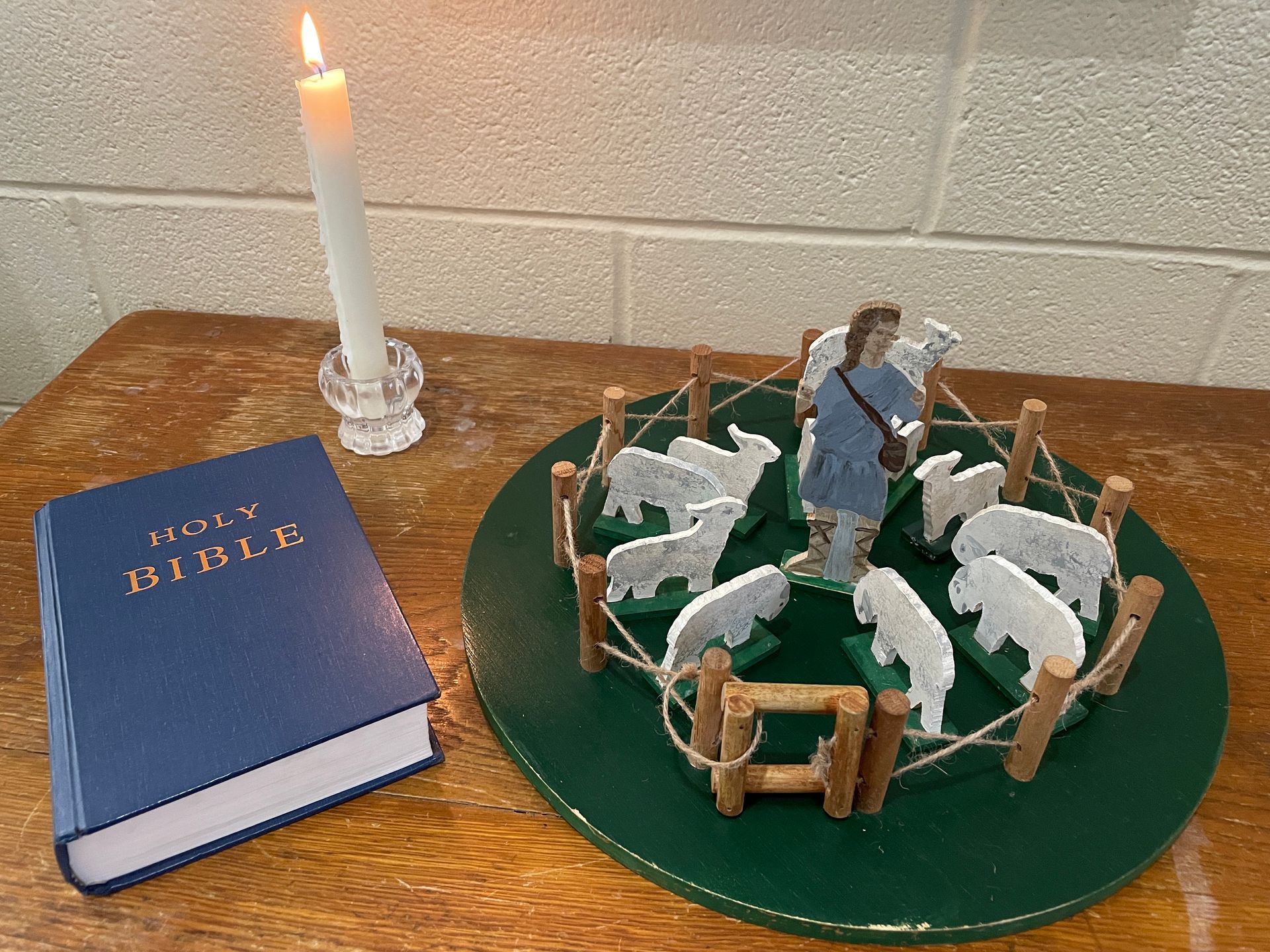 A blue bible is sitting on a wooden table next to a model of a shepherd and sheep.