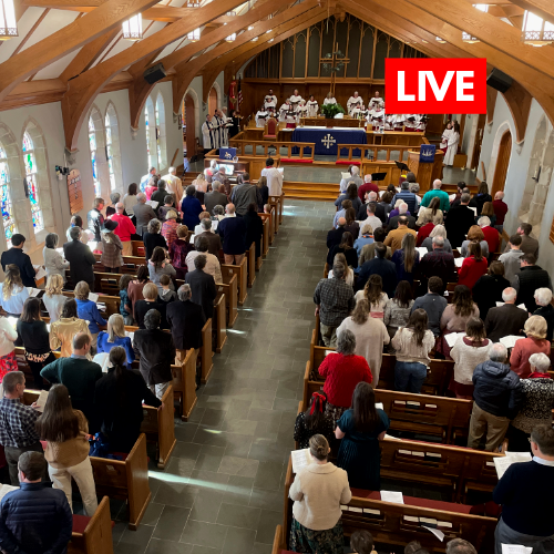 A large group of people are sitting in a church with a live sign on the ceiling.