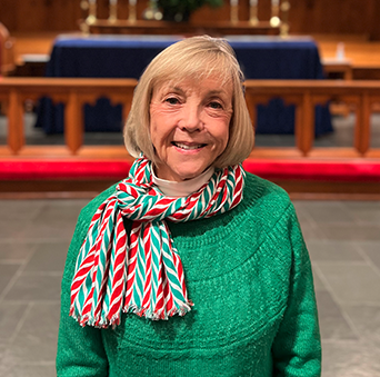 A woman wearing a green sweater and a scarf is standing in front of an altar in a church.