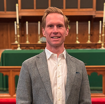 A man in a suit and white shirt is standing in front of a church altar.