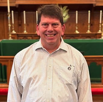 A man in a plaid shirt is smiling in front of a church altar.