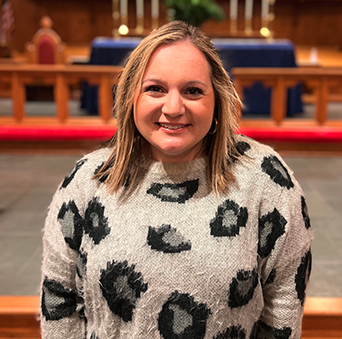A woman in a leopard print sweater is smiling in front of a church altar.