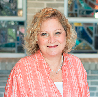 A woman in a pink striped shirt is smiling for the camera in front of a stained glass window.