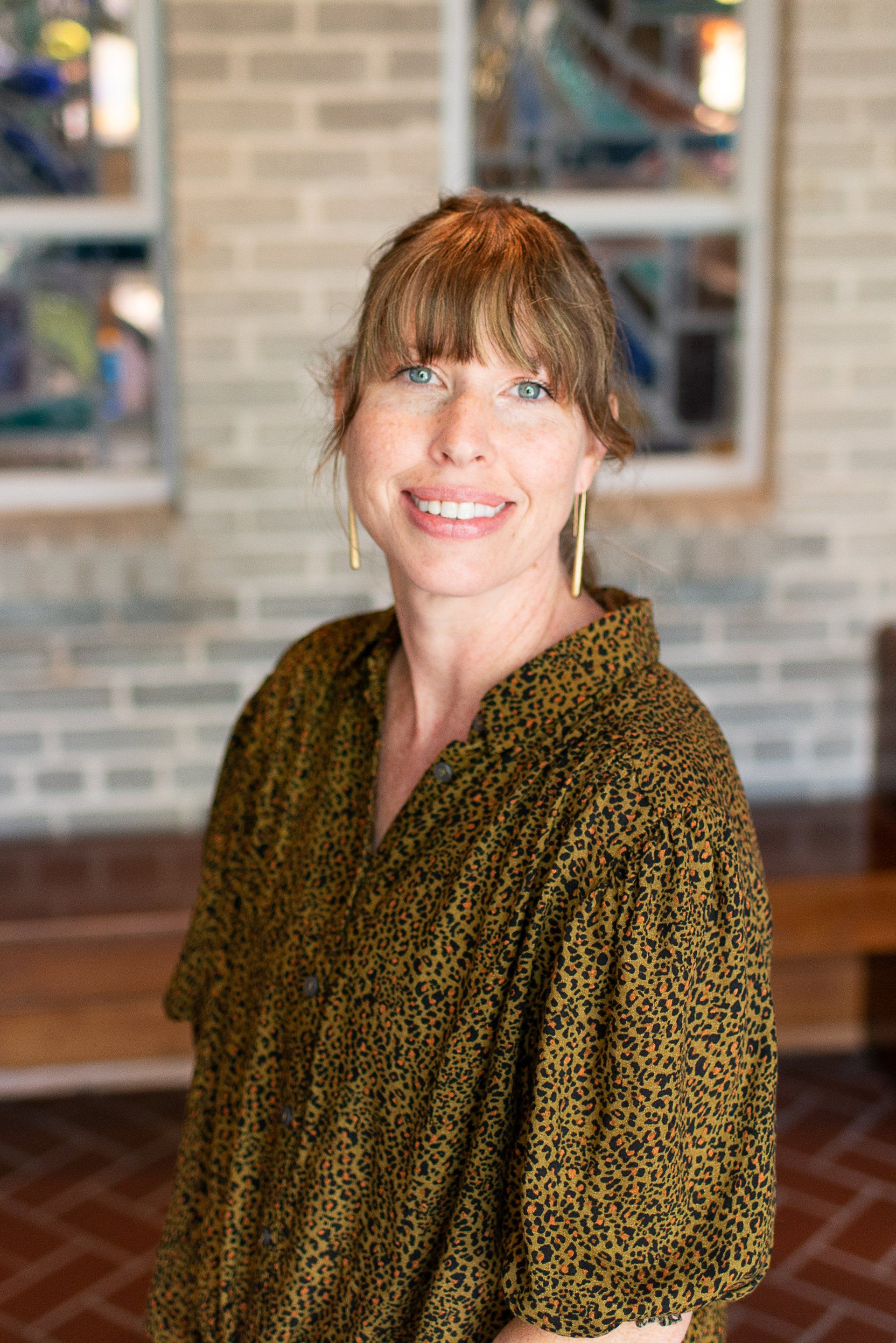 A woman in a red shirt is smiling in front of a stained glass window.
