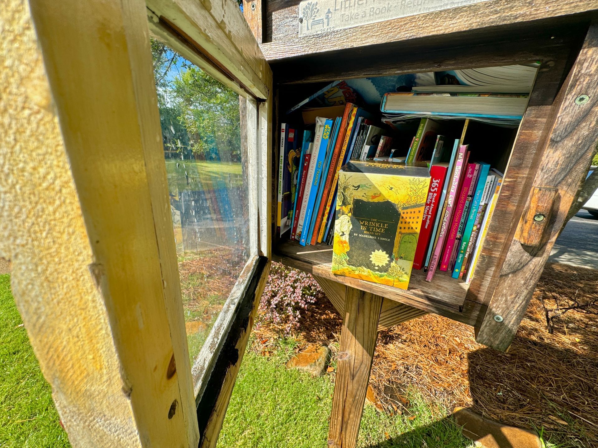 A wooden box filled with books is sitting in the grass.