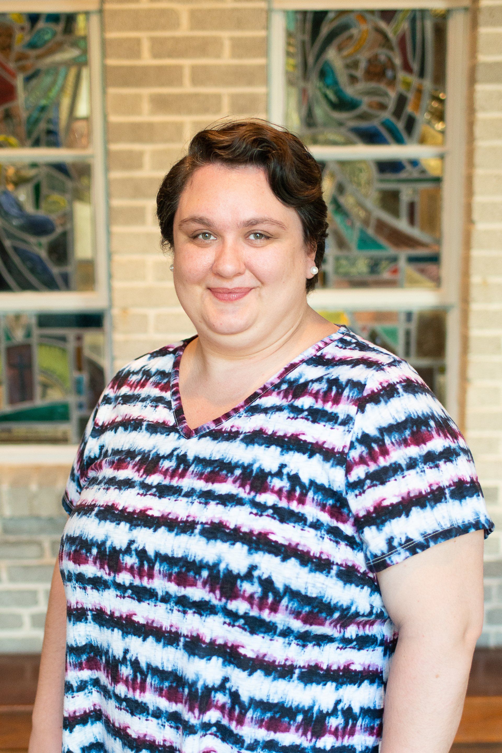 A woman in a striped shirt is standing in front of a stained glass window.