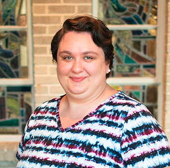 A woman in a striped shirt is smiling in front of a stained glass window.