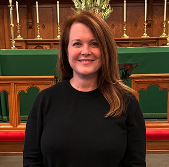 A woman in a black sweater is standing in front of an altar in a church.