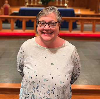 A woman wearing glasses is standing in front of an altar in a church.