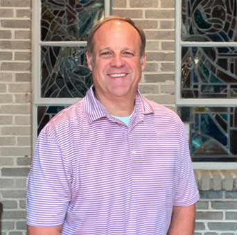 A man in a striped shirt is standing in front of a brick wall.