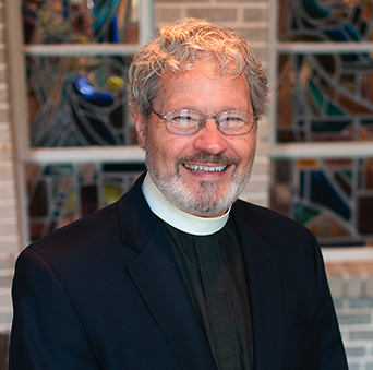 A man in a suit and tie is smiling in front of a stained glass window.