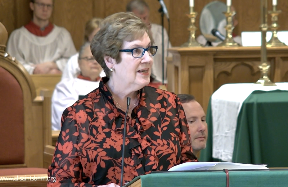 A woman wearing glasses is speaking into a microphone in a church