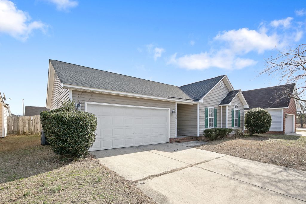 Tan house with a two-car garage, a driveway, and a small front yard under a blue sky.