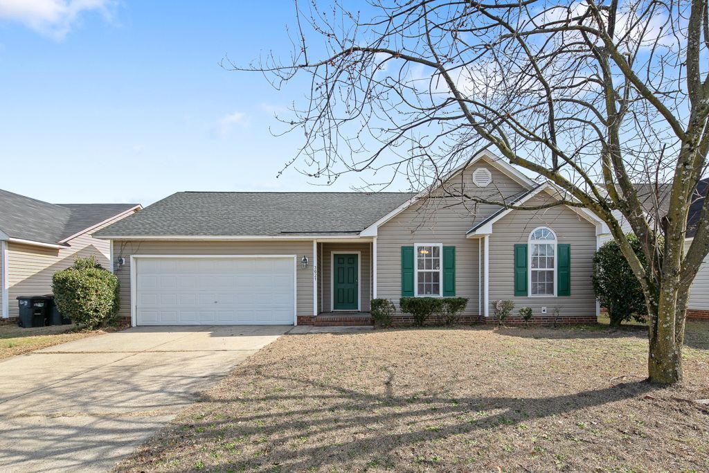 Tan, one-story house with green shutters and door. Driveway and bare tree in front.