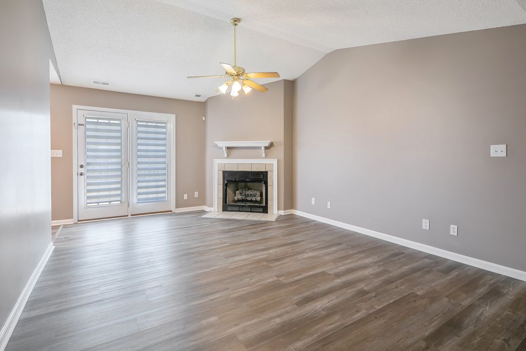 Empty living room with fireplace, doors, ceiling fan, and gray walls.