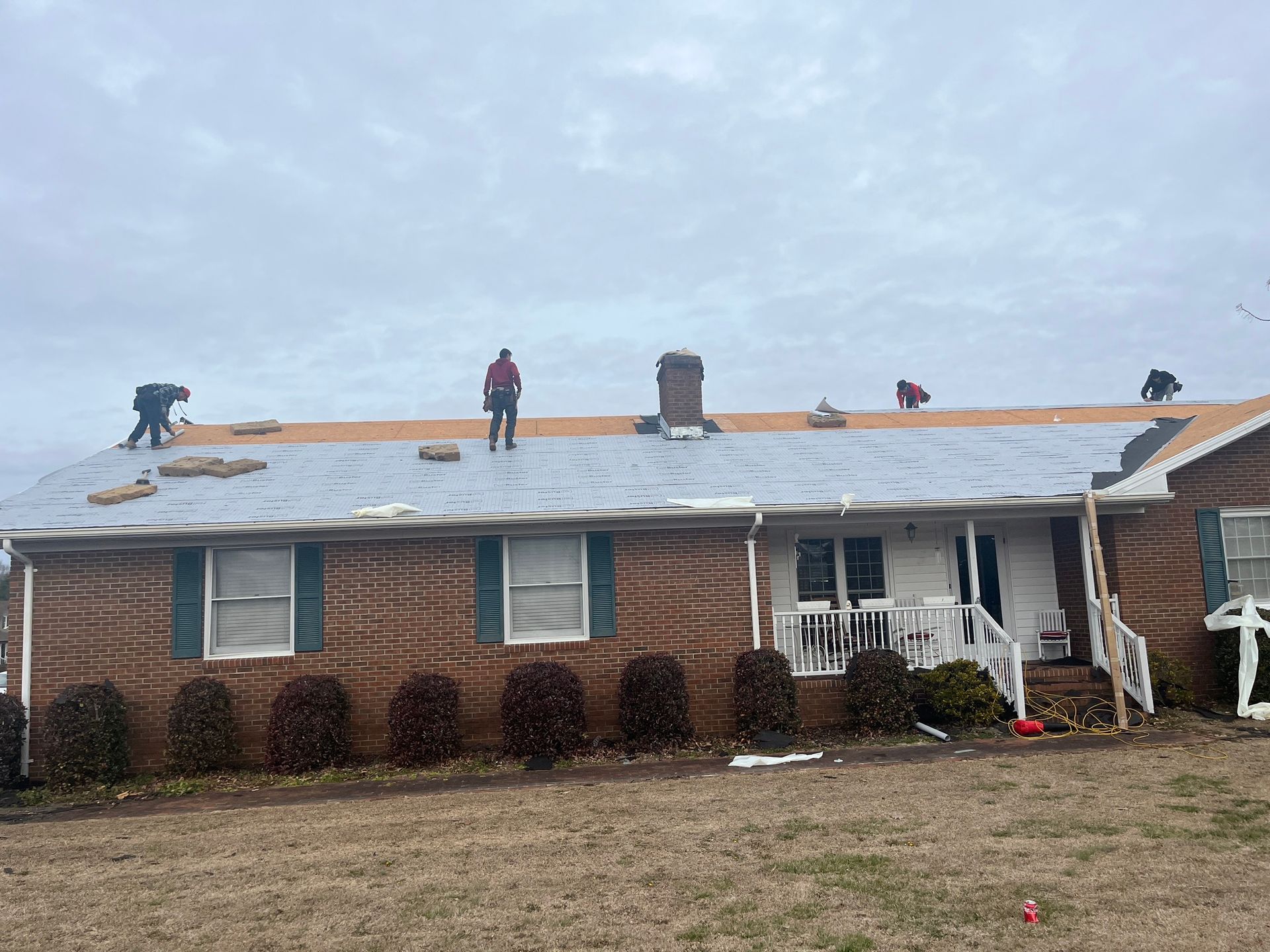 A group of people are working on the roof of a brick house.