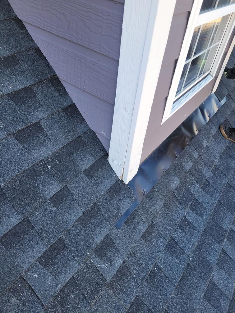 A person is standing on a roof next to a house with a window.