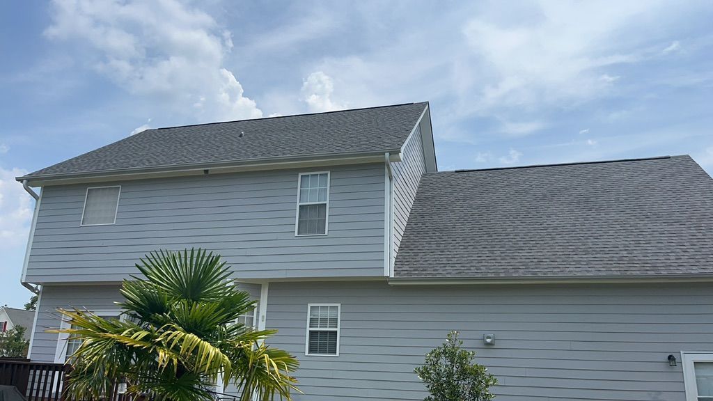 A large white house with a gray roof and a palm tree in front of it.