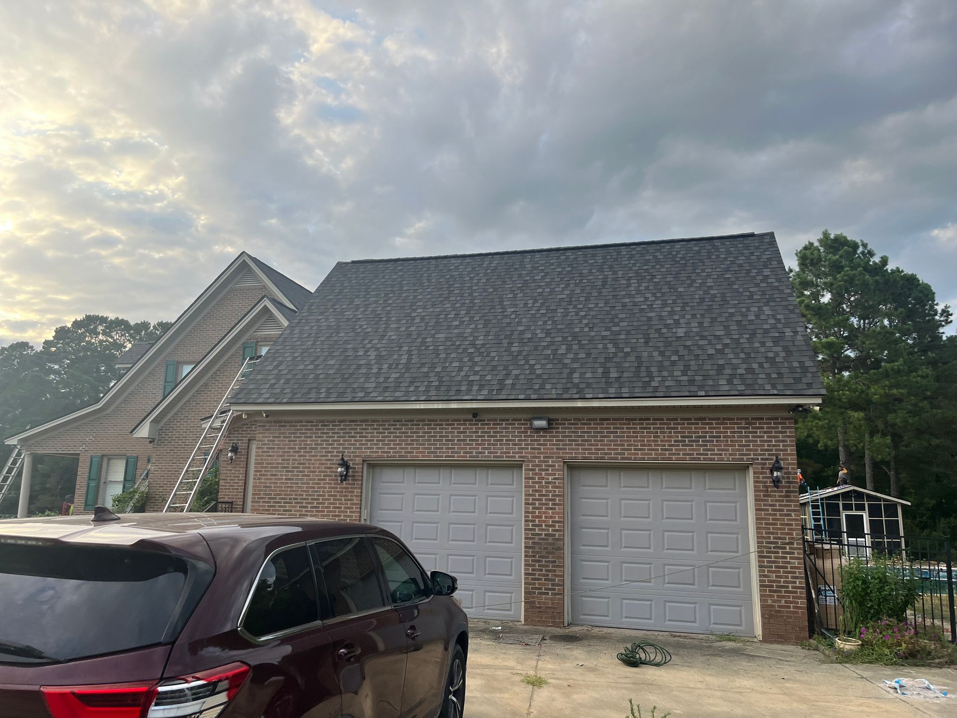 A car is parked in front of a brick house with two garage doors.