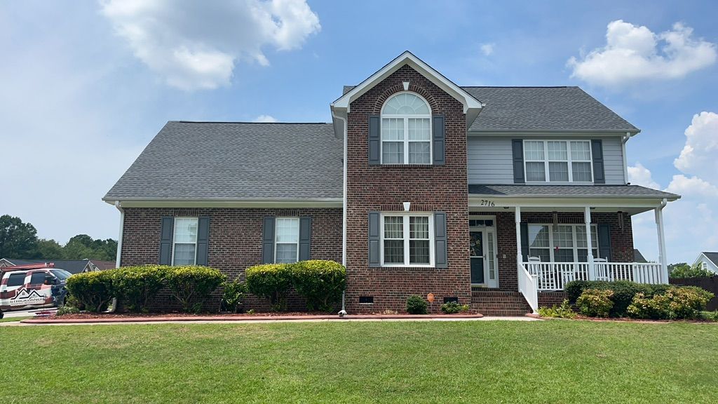 A large brick house with a gray roof is sitting on top of a lush green lawn.