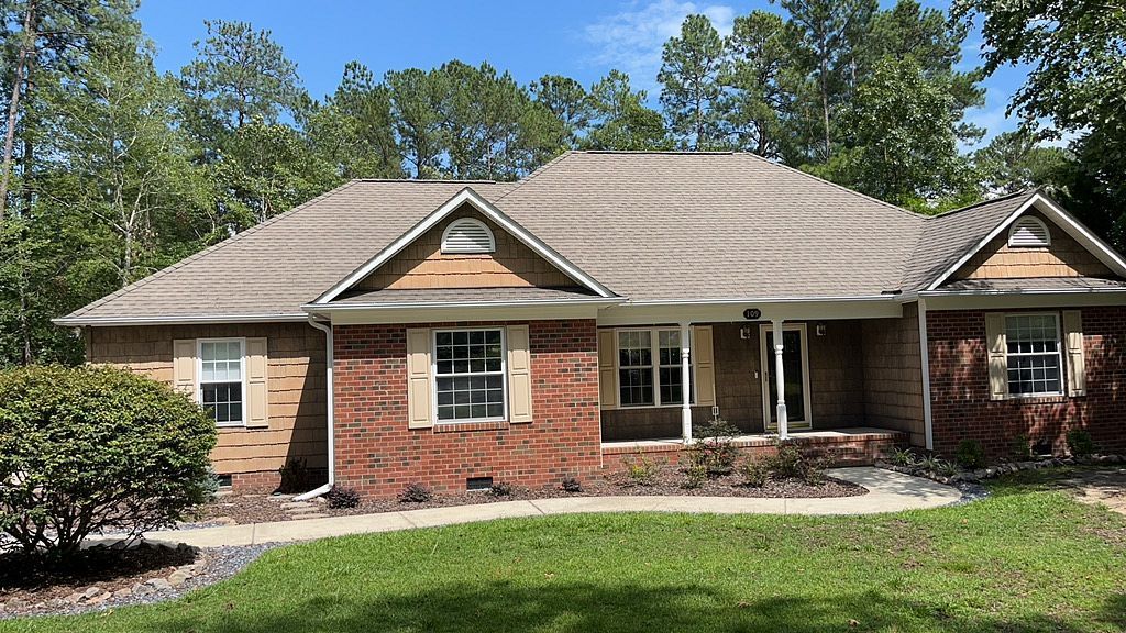 A large brick house with a porch and a roof surrounded by trees.