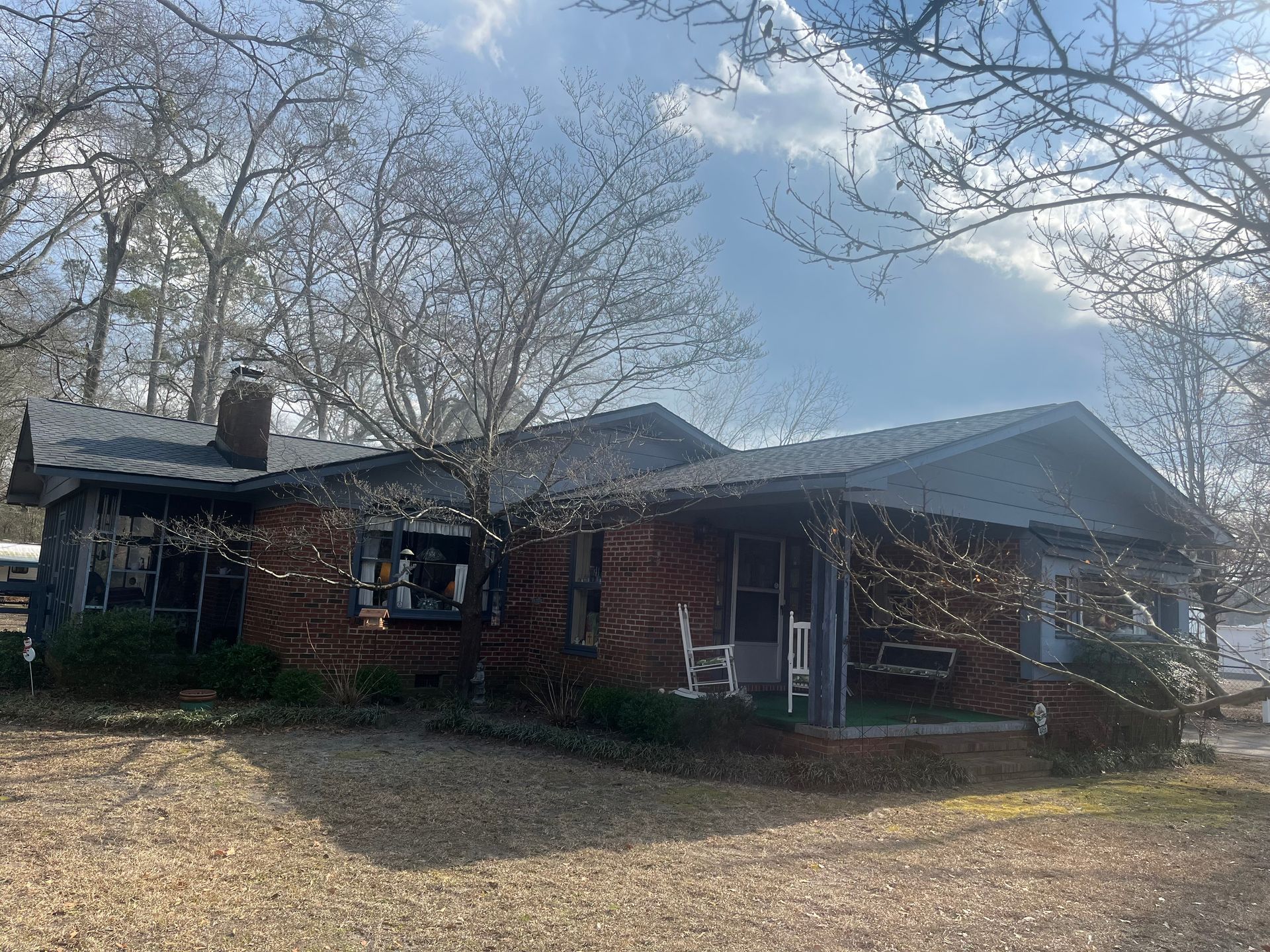 Brick house with porch and dark roof, under a bright blue sky with bare tree branches.