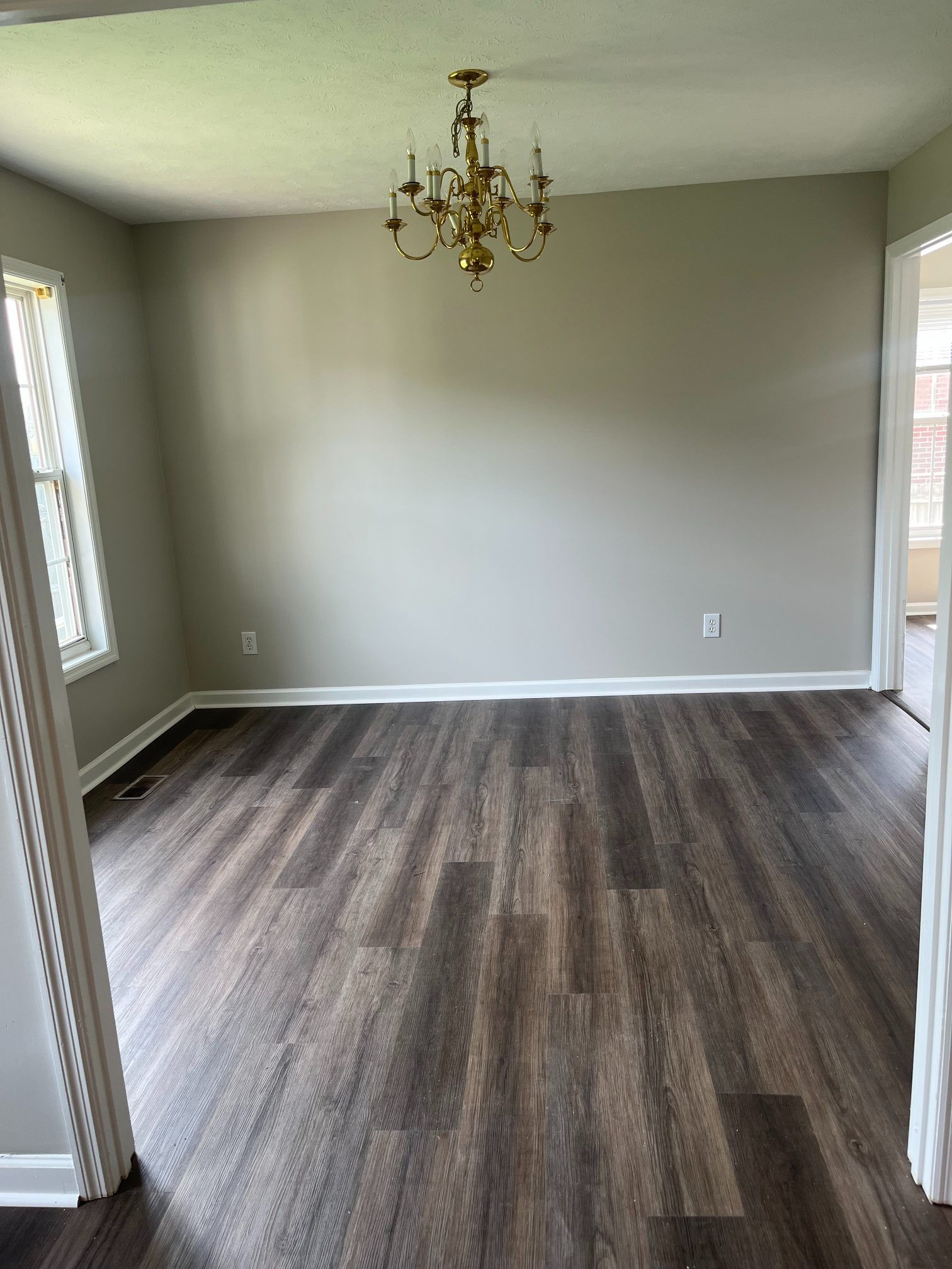 Empty room with dark wood-look flooring, beige walls, and a gold chandelier.