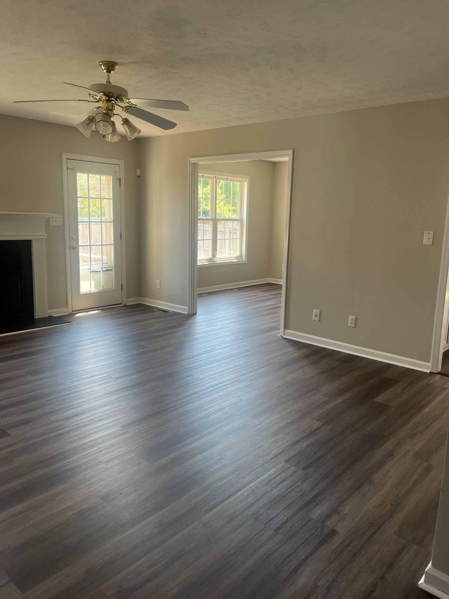 Spacious living room with dark wood-look flooring, neutral walls, and a view into another room.