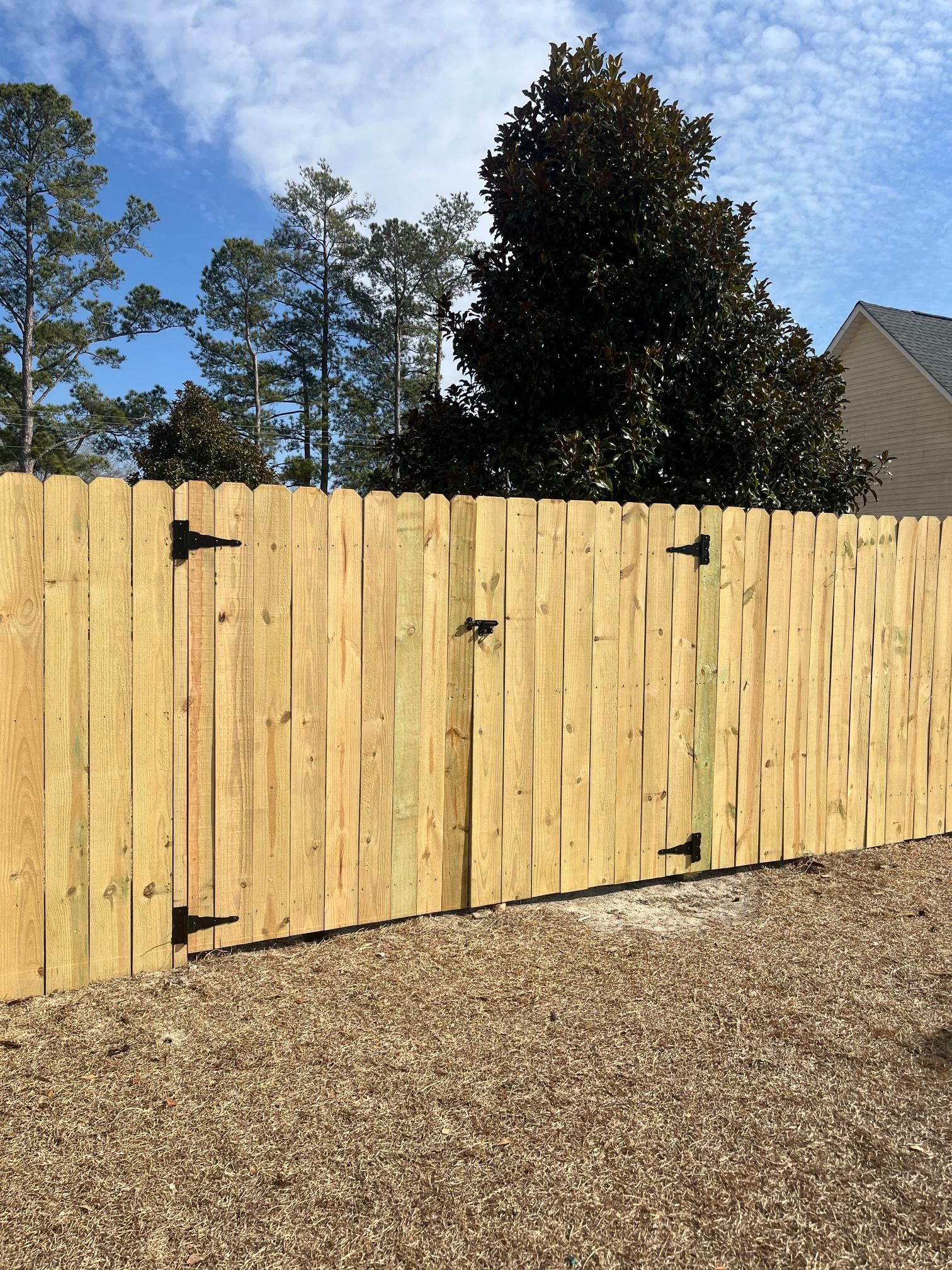 Wooden fence with gate, hinges, and gravel ground under a blue sky.