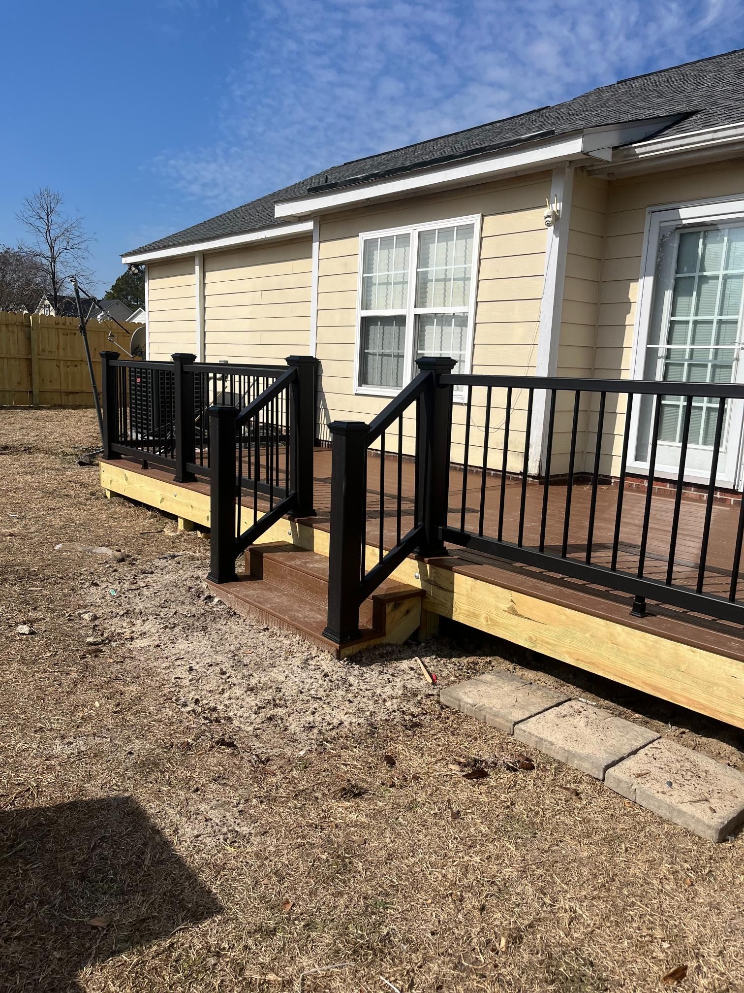 A new wooden deck with black railings next to a yellow house under a blue sky.