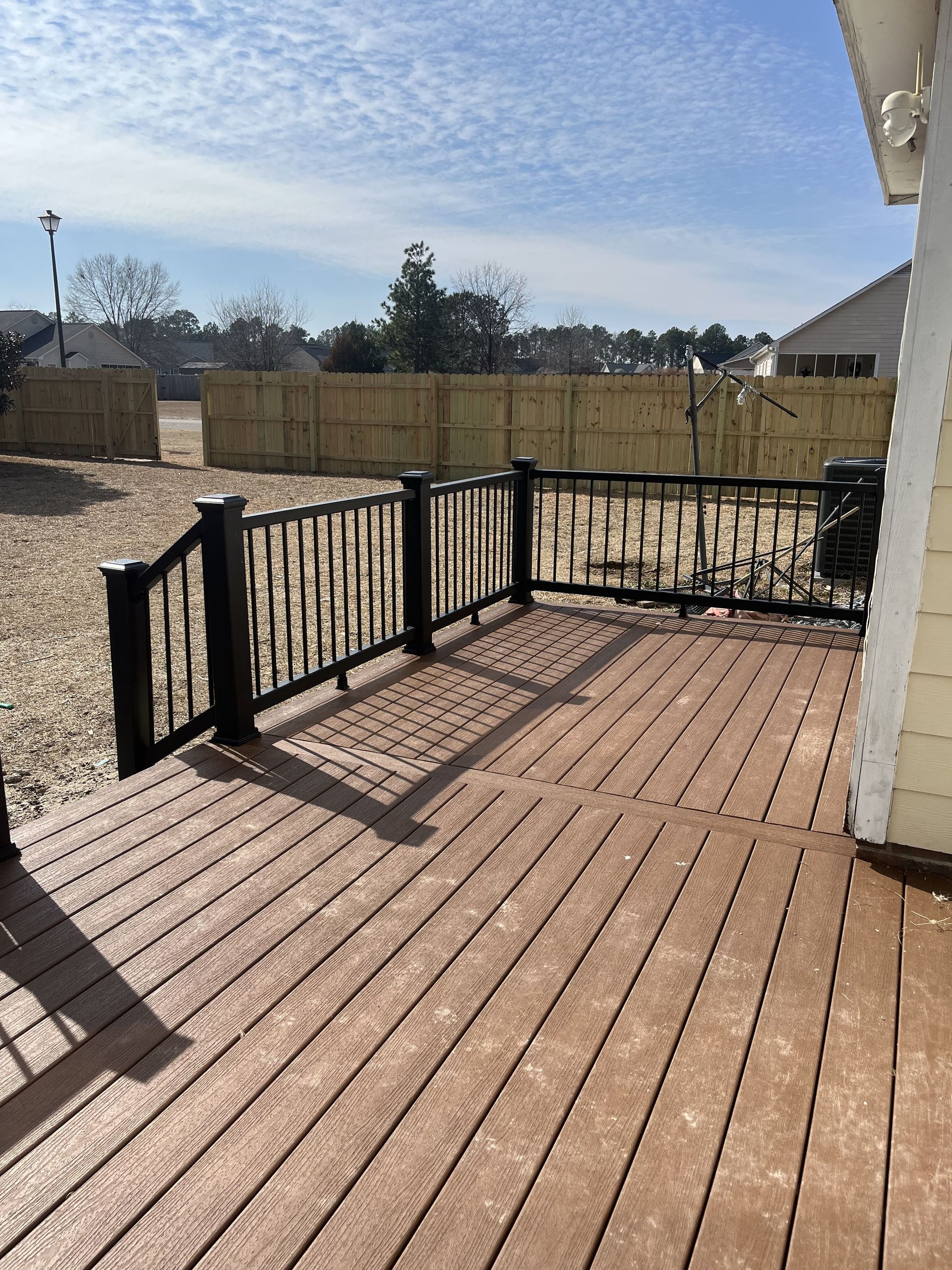 Brown wooden deck with black railing on a sunny day. Backyard with a wooden fence.