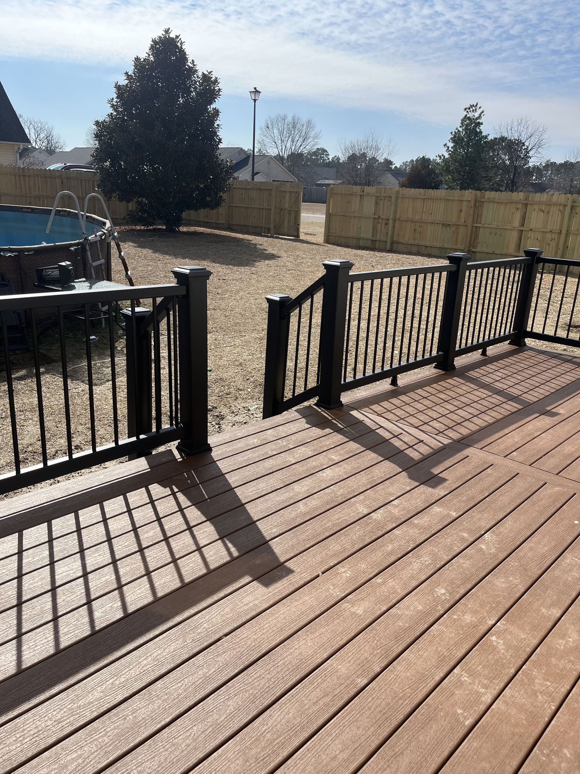 Wooden deck with black railings overlooking a gravel yard with a pool and a bamboo fence.