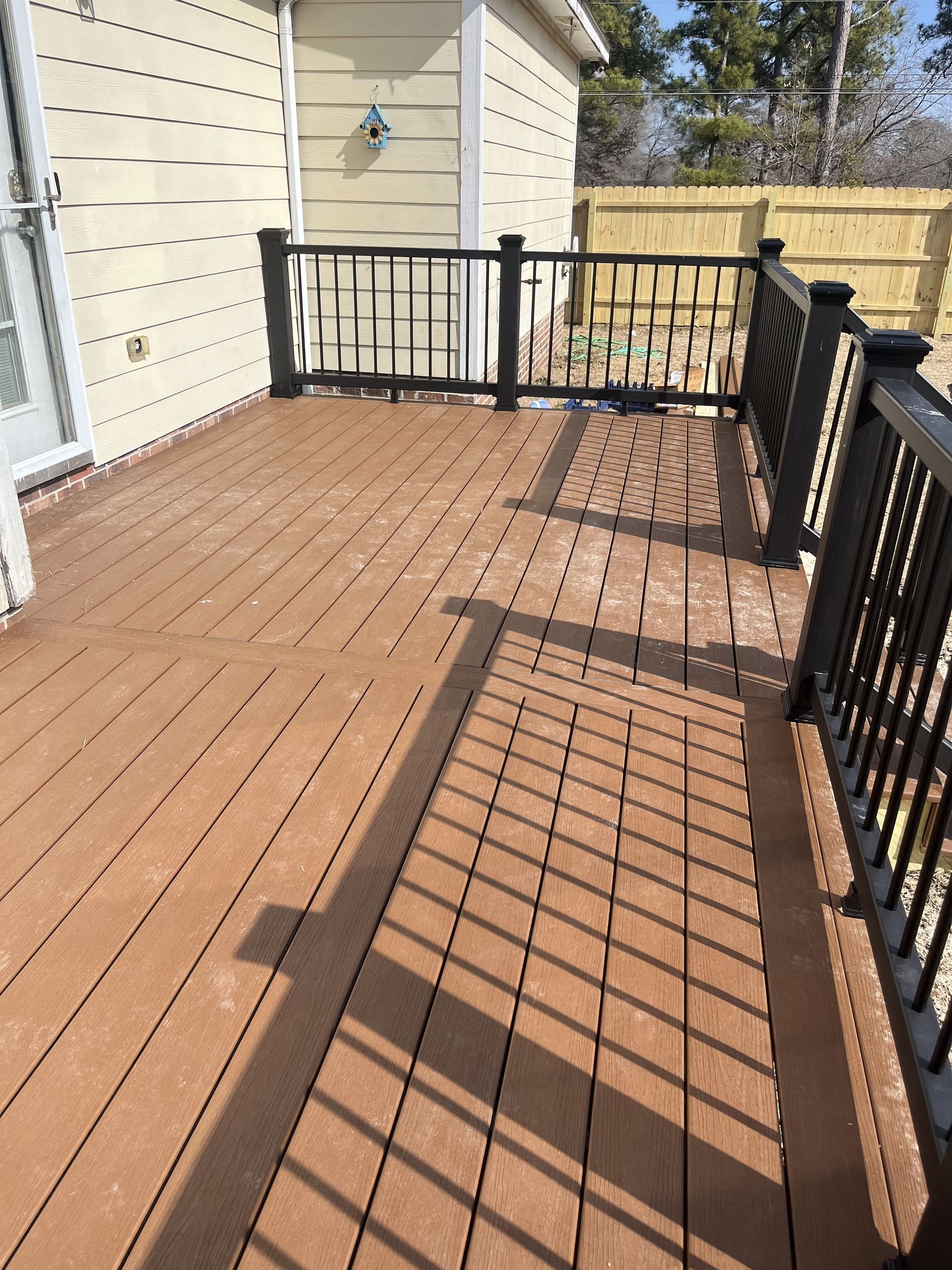 Brown wooden deck with black railings and a light-colored building in the background.