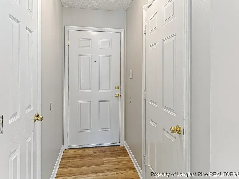 Narrow hallway with white doors, light gray walls, and wood-look flooring.