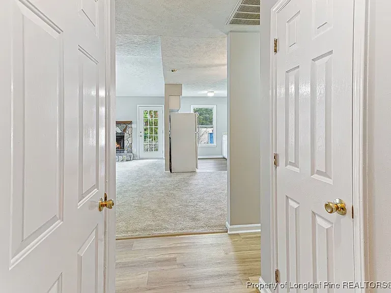 View through open white doors into a home's interior, showing a living room with a fireplace and windows.