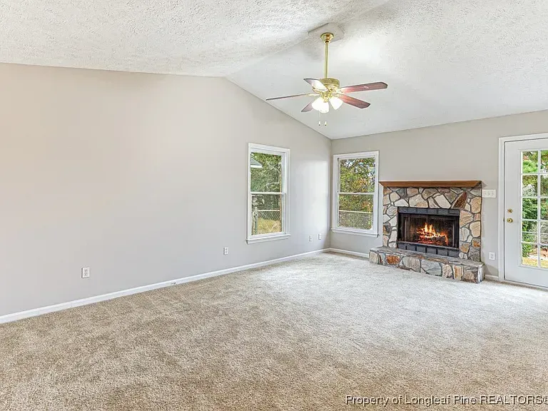 Living room with fireplace, windows, and tan carpet. Gray walls and vaulted ceiling.