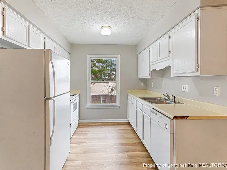 White kitchen with cabinets, appliances, and a window. Light wood floor and off-white countertops.