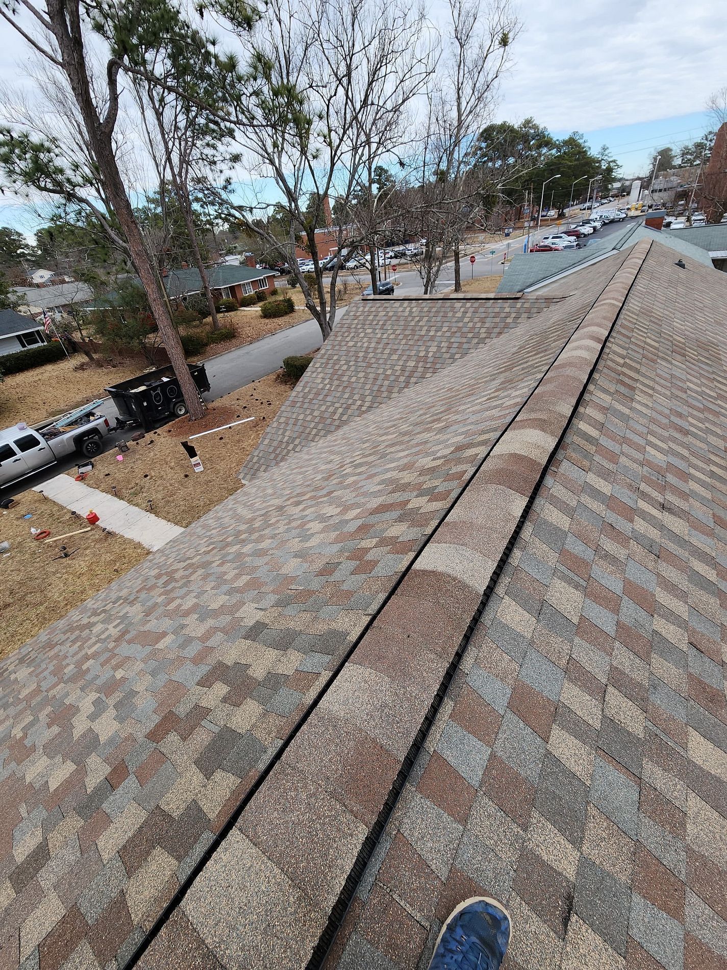 View from a roof of a neighborhood street; brown asphalt shingles, blue sky.
