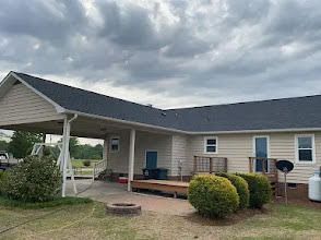 Beige house with a carport and black roof under a cloudy sky.