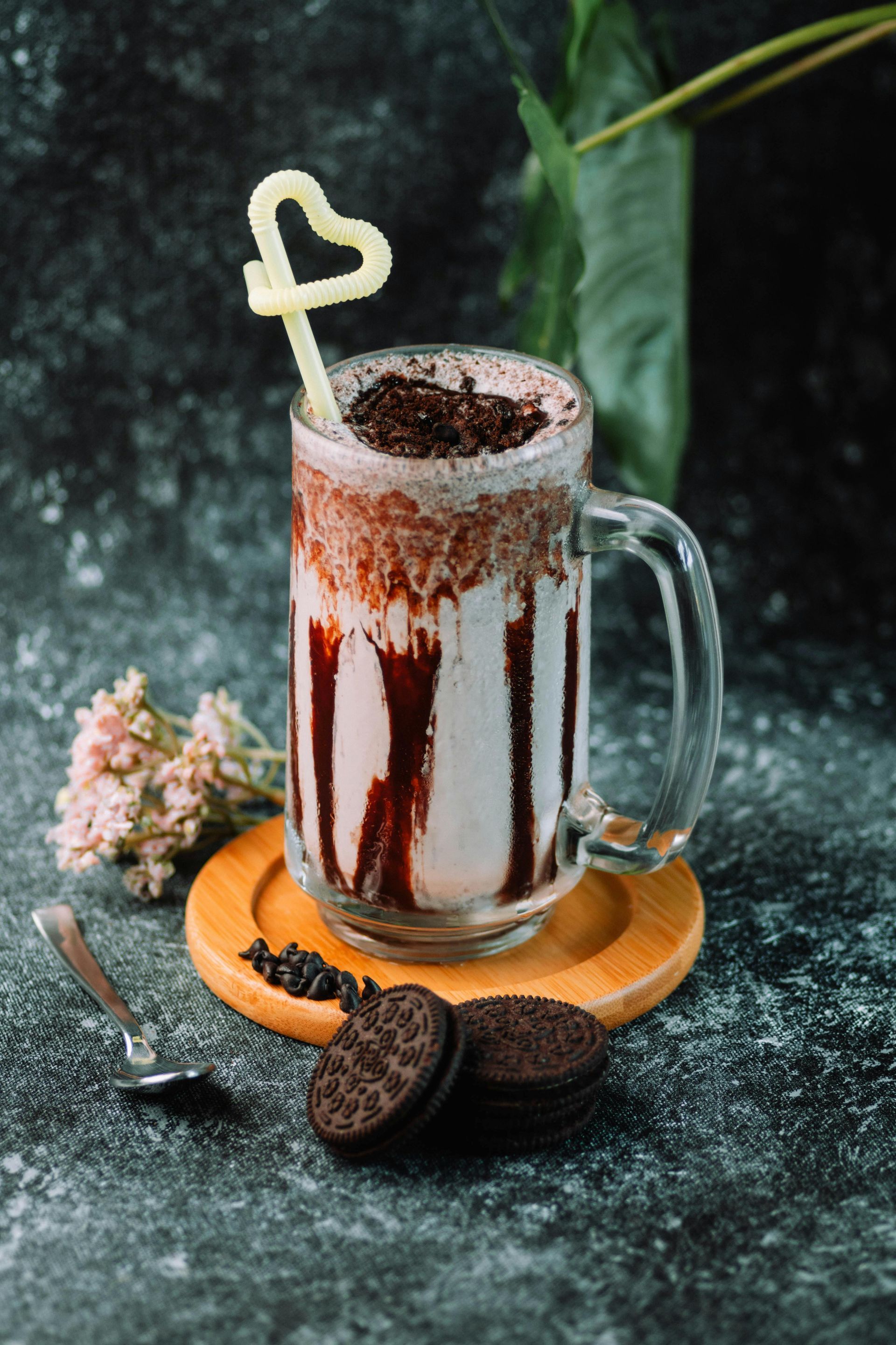 A milkshake with a heart shaped straw and oreo cookies on a table.