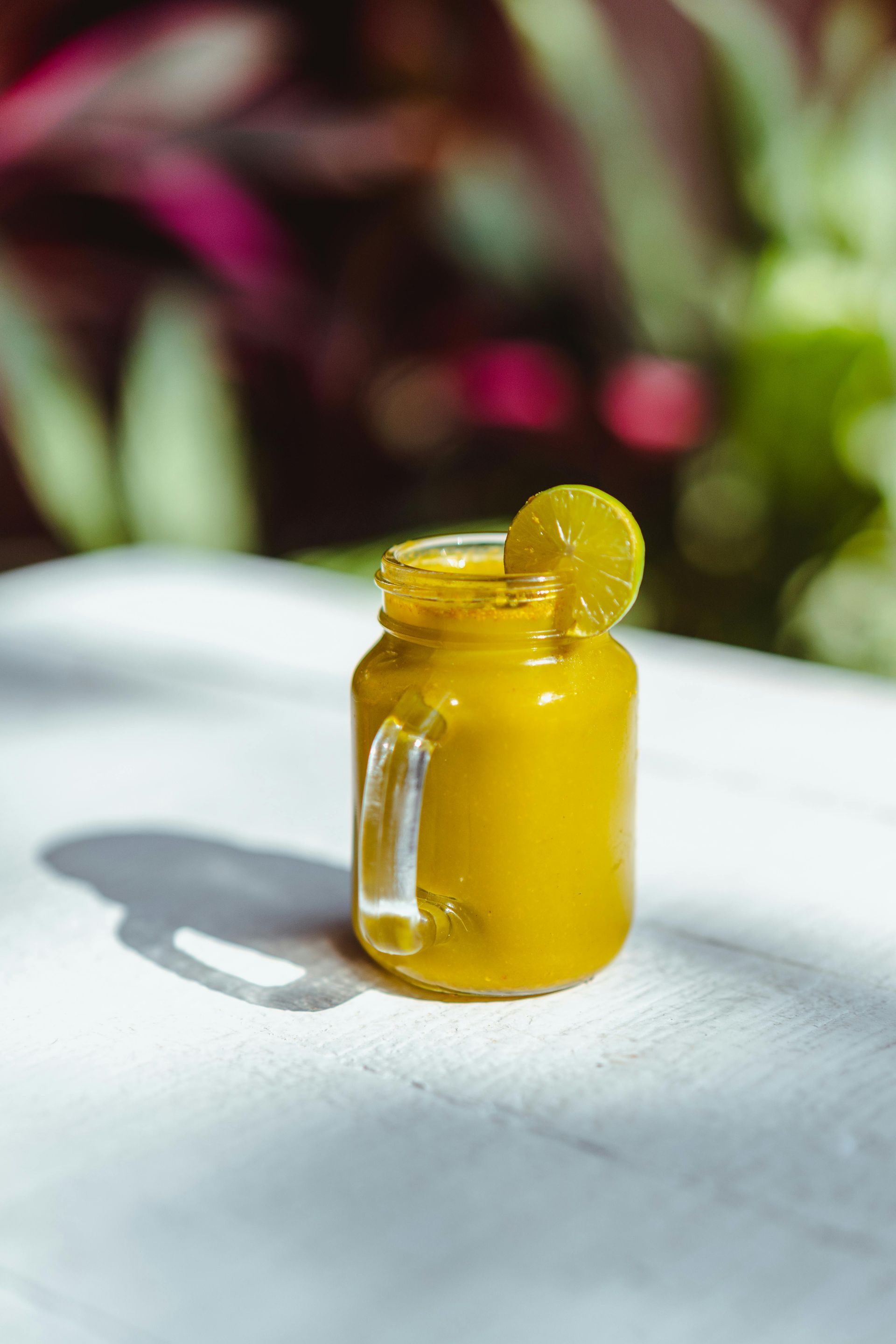 A small mason jar filled with a yellow liquid and a lemon slice on a table.