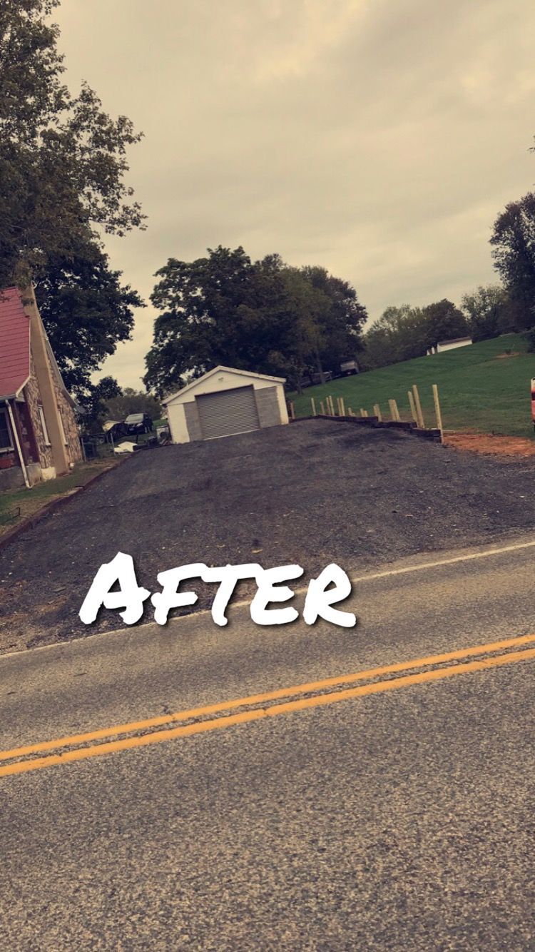 Paved asphalt driveway in front of a white garage, and a road. Cloudy sky, trees.