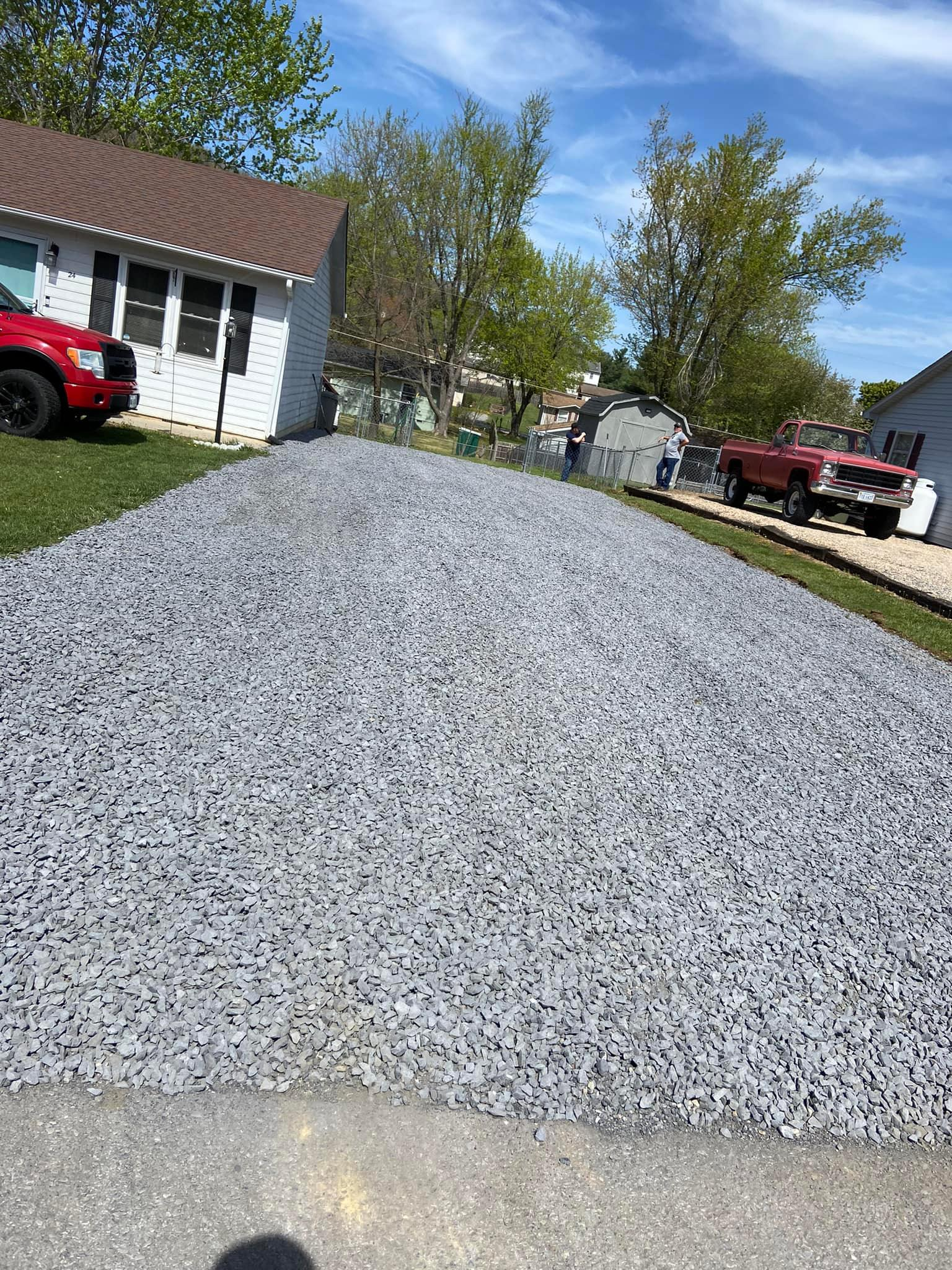 Gravel driveway in front of a white house with a red truck parked in the yard.