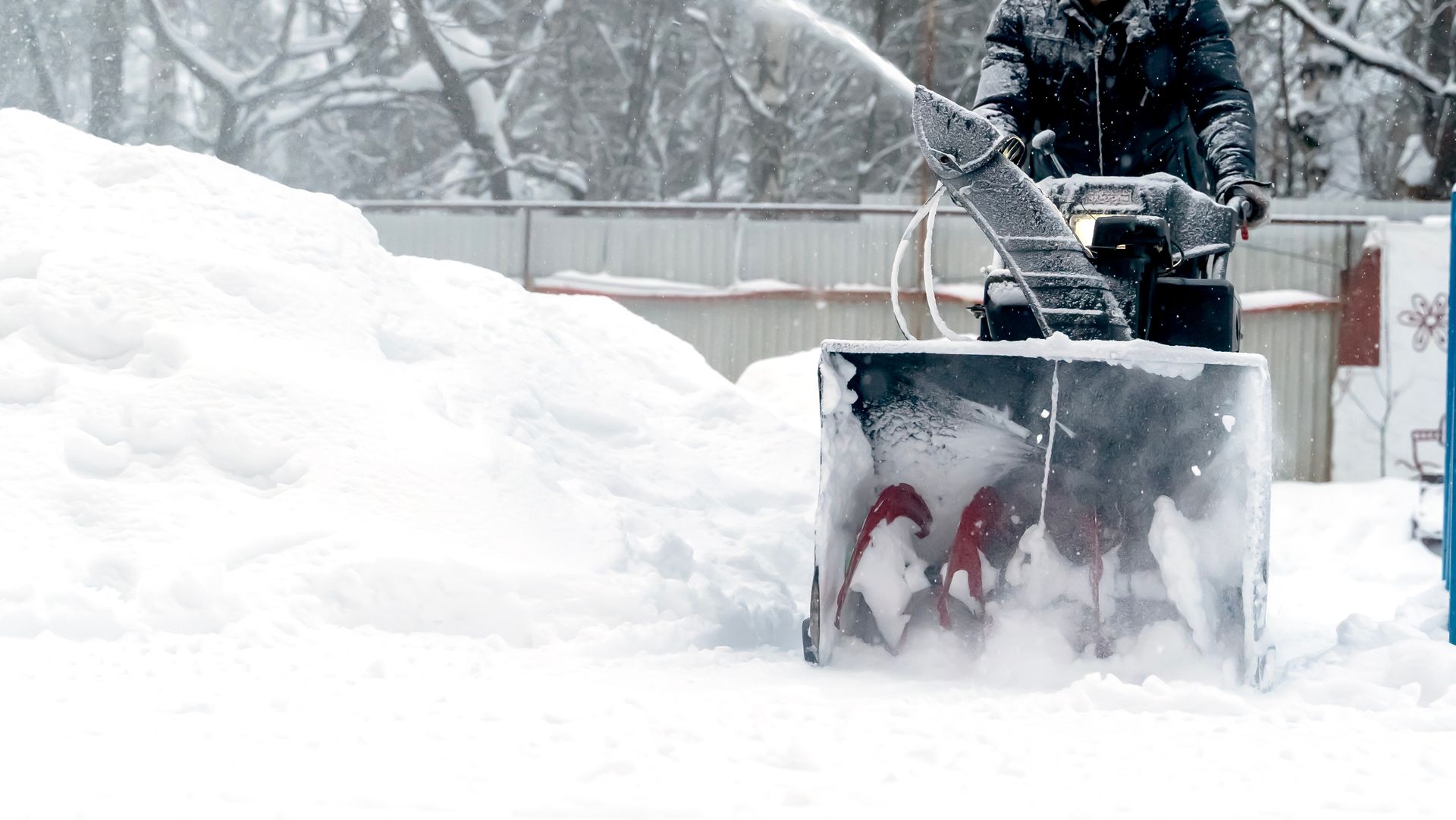 Person using a snowblower in a snowy outdoor setting, clearing a large pile of snow.