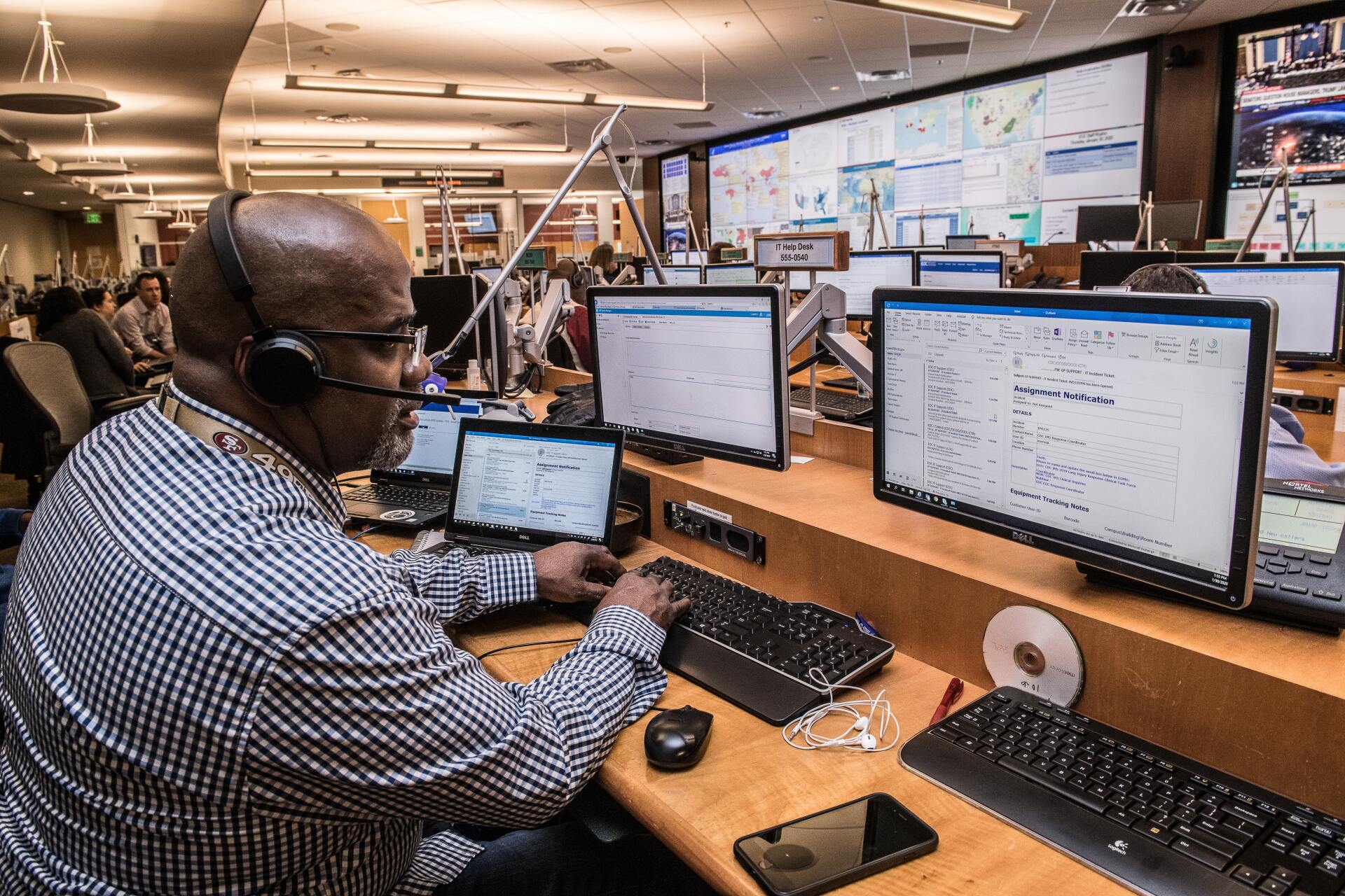 man working in 911 dispatch office looking at computer screens while using a phone headset