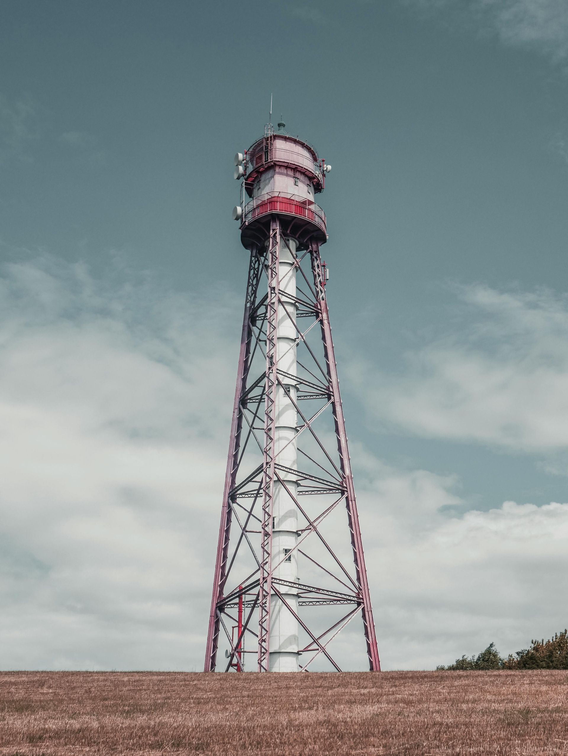 A tall red and white tower is sitting on top of a grassy hill.