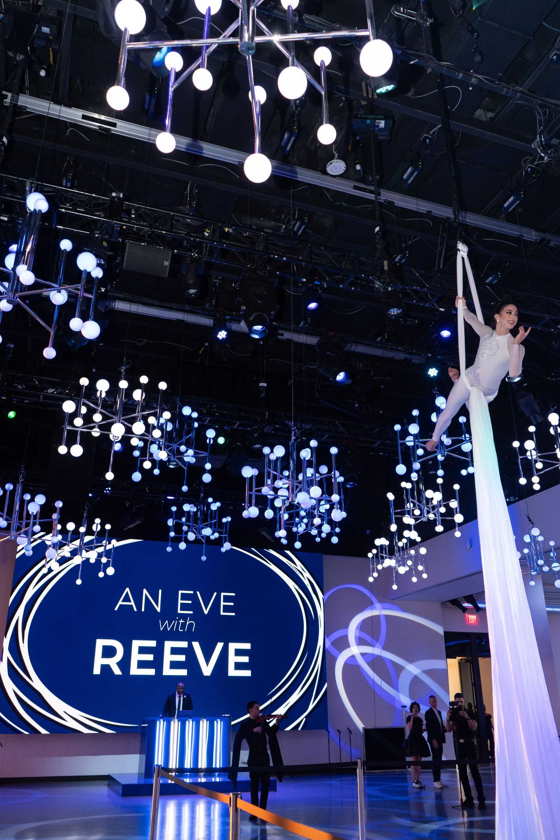 An aerial performer is performing in front of a large screen that says an eve with reeve