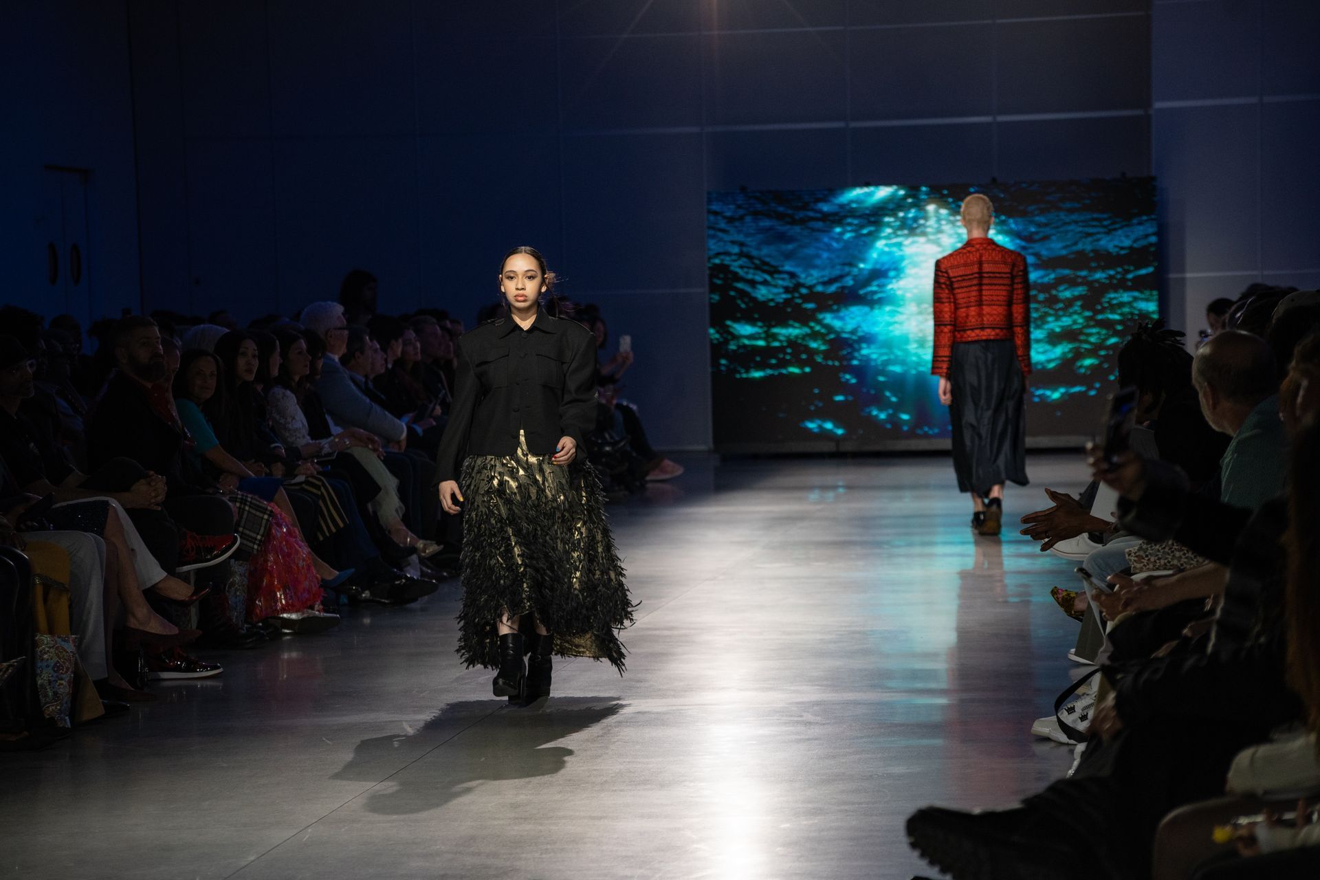 Two models are walking down the runway at a fashion show.