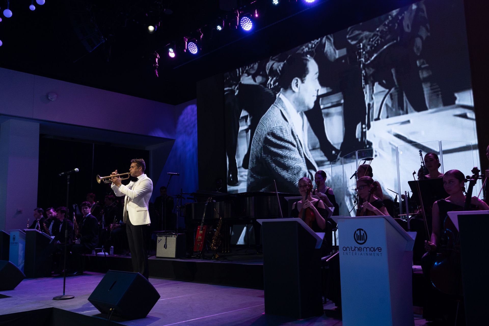 A man is playing a trumpet on a stage in front of an orchestra.