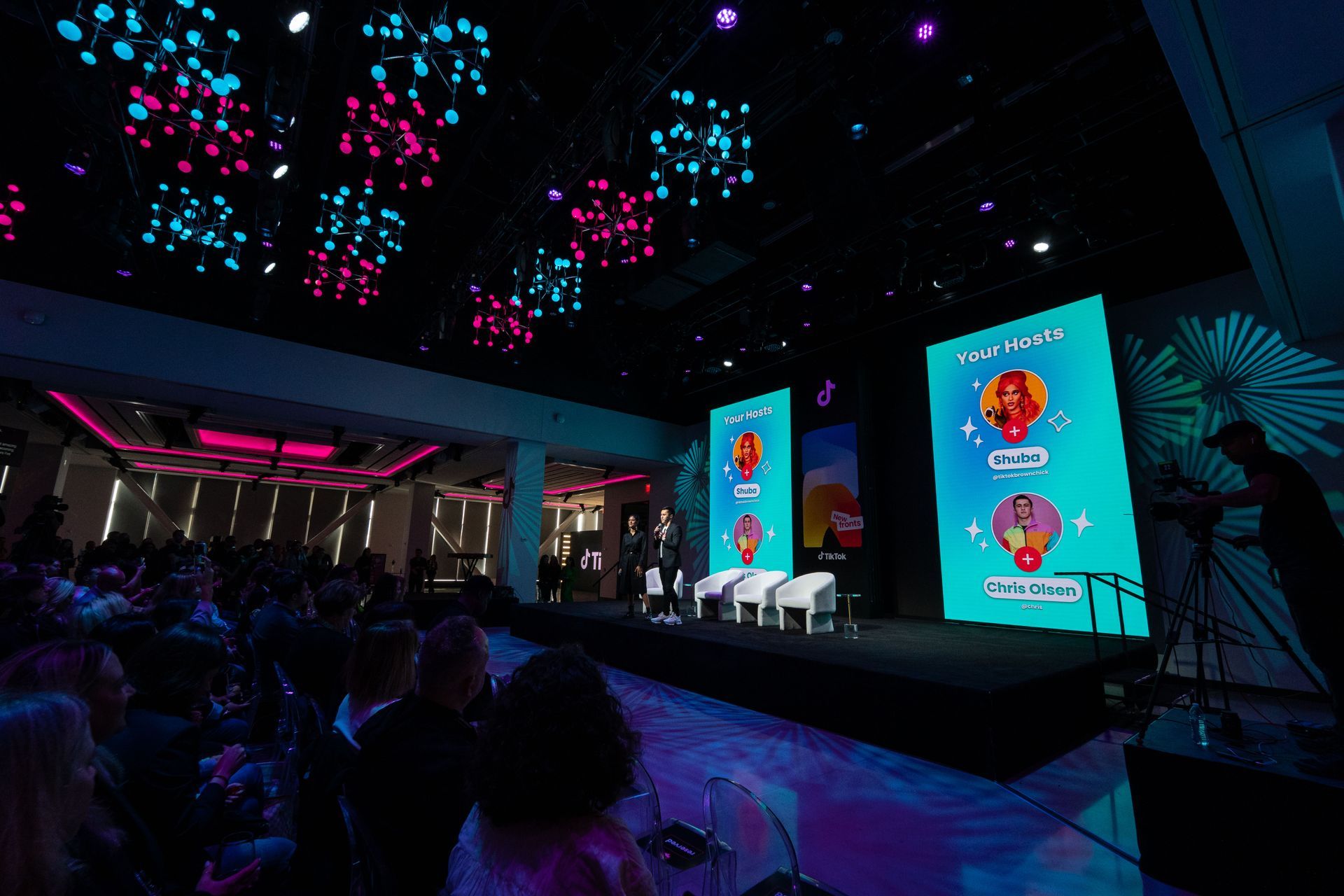 A crowd of people are sitting in front of a stage in a large room.